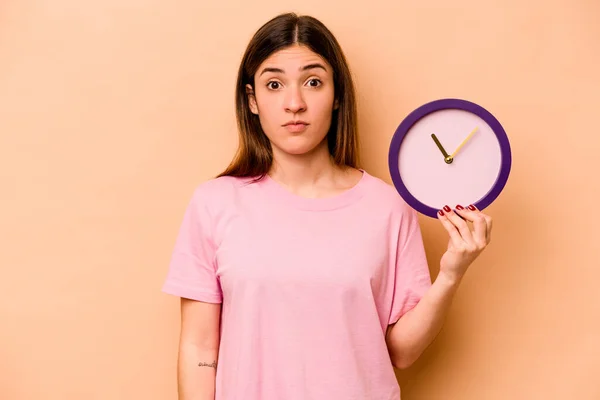 Mujer Hispana Joven Sosteniendo Reloj Aislado Sobre Fondo Beige Encoge —  Fotos de Stock