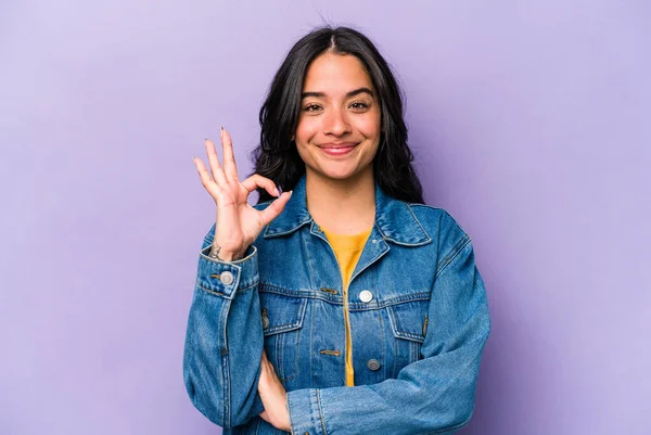 Mor arka planda izole edilmiş genç İspanyol kadın bir göz kırptı ve elleriyle iyi bir jest yaptı..