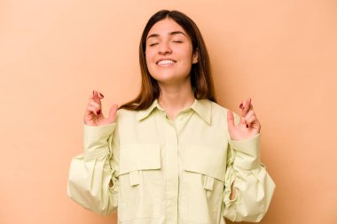 Latin kökenli genç bir kadın, şans dilemek için bej arka planda izole edilmiş.