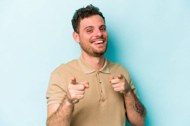Mavi arka planda izole edilmiş genç beyaz adam parmaklarıyla ön tarafı işaret ediyor..