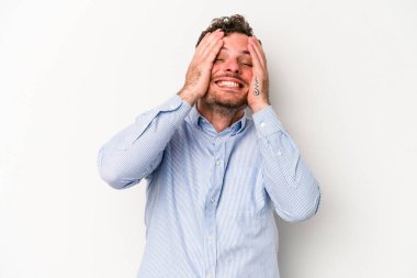 Beyaz arka planda izole olmuş genç beyaz bir adam ellerini başının üstünde tutarak neşeyle gülüyor. Mutluluk kavramı.