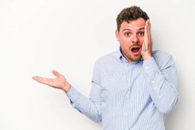 Beyaz arka planda izole edilmiş genç beyaz adam, avuç içi fotokopi alanını elinde tutmaktan etkilenmiş..