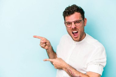 Mavi arka planda izole edilmiş genç beyaz adam işaret parmağıyla fotokopi alanını işaret ederek heyecan ve arzusunu ifade ediyor..