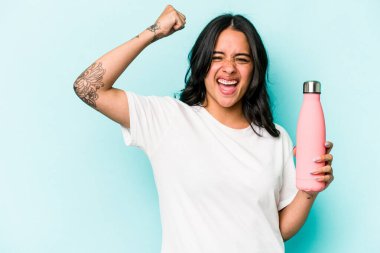 Mavi arka planda termosu olan genç İspanyol kadın zafer kazandıktan sonra yumruğunu kaldırıyor..