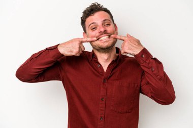 Beyaz arka planda izole edilmiş genç beyaz adam gülümsüyor, parmaklarını ağıza doğrultuyor..