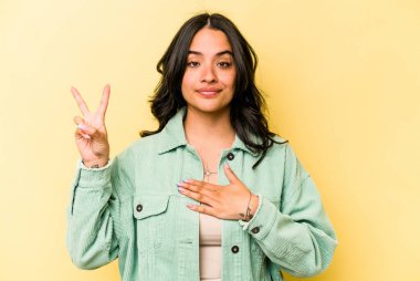 Sarı arka planda izole edilmiş genç İspanyol kadın yemin ediyor, elini göğsüne koyuyor..