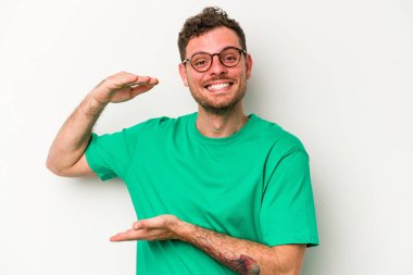 Beyaz arka planda izole edilmiş genç beyaz bir adam işaret parmaklarıyla küçük bir şey tutuyor, gülümsüyor ve kendinden emin..