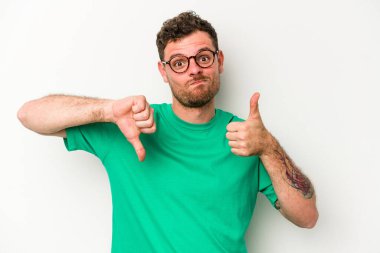 Beyaz arka planda izole edilmiş genç beyaz bir adam baş parmaklarını aşağı ve yukarı kaldırıyor, zor seçim konsepti
