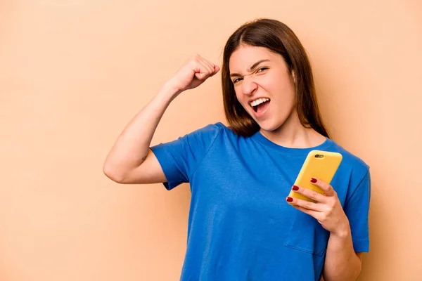 Mladá Běloška Drží Mobilní Telefon Izolovaný Béžovém Pozadí Zvedající Pěst — Stock fotografie