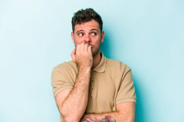 Mavi arka planda izole edilmiş, tırnak yiyen, gergin ve endişeli genç bir beyaz adam..