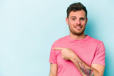 Mavi arka planda izole edilmiş genç beyaz adam yan tarafı işaret ediyor.