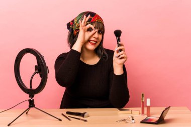 Makyaj yapan genç bir kadın pembe arka planda izole edilmiş makyaj dersi veriyor..