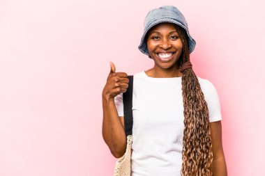 Genç Afrikalı Amerikalı bir kadın pembe arka planda izole bir şekilde kumsala gidiyor gülümsüyor ve başparmağını kaldırıyor.