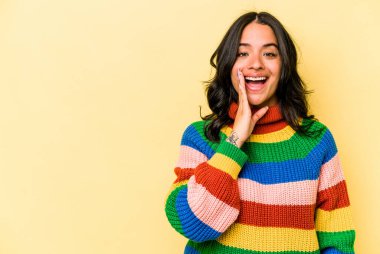 Sarı arka planda izole edilmiş genç İspanyol kadın yüksek sesle bağırıyor, gözleri açık ve elleri gergin tutuyor..