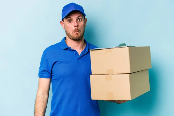 Young Caucasian Delivery Man Isolated Blue Background Shrugs Shoulders Open — стоковое фото
