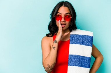 Mavi arka planda izole edilmiş plaj havlusu tutan genç İspanyol kadın gizli bir sıcak fren haberi veriyor ve yana bakıyor.