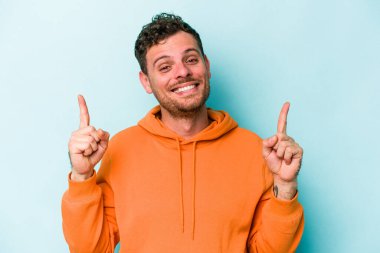 Mavi arka planda izole genç beyaz adam işaret iki ön parmakları boş bir boşluk gösteren.