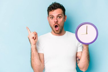 Kafkasyalı genç bir adam mavi arka planda izole edilmiş bir saat tutuyor.