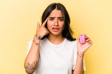 Pembe arka planda izole edilmiş anahtar taşıyan Latin kökenli genç bir kadın işaret parmağıyla yaptığı hayal kırıklığı jestini gösteriyor..