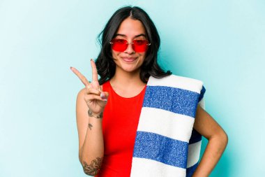 Elinde plaj havlusu tutan genç İspanyol kadın mavi arka planda iki numarayı parmaklarıyla gösteriyor..