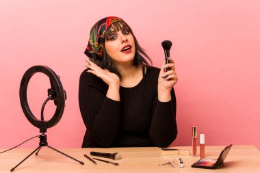 Makyaj öğretmeni olan genç bir kadın pembe arka planda izole edilmiş, şaşırmış ve şok olmuş..