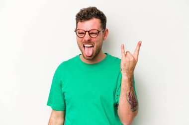 Beyaz arka planda izole edilmiş genç beyaz bir adam parmaklarıyla kaya hareketi gösteriyor.