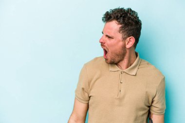 Kafkasyalı genç adam mavi arka planda izole edilmiş. Çok kızgın, öfkeli, hayal kırıklığına uğramış..