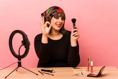 Makyaj öğretmeni olan genç bir kadın pembe arka planda izole edilmiş neşeli ve kendinden emin bir şekilde iyi bir jest yapıyor..