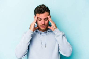 Kafkasyalı genç bir adam mavi arka planda izole edilmiş, başı ağrıyor, yüzüne dokunuyor..