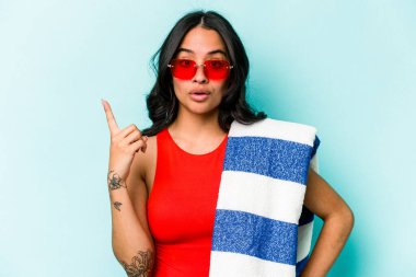 Mavi arka planda izole edilmiş plaj havlusu tutan genç İspanyol kadının harika bir fikri var, yaratıcılık kavramı..