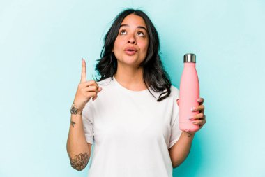 Mavi arka planda termo tutan genç İspanyol kadın ağzı açık bir şekilde üst tarafı işaret ediyor..