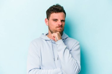 Kafkasyalı genç adam mavi arka planda izole edilmiş düşünüyor ve bakıyor, yansıtıyor, düşünüyor, bir fantezi kuruyor..