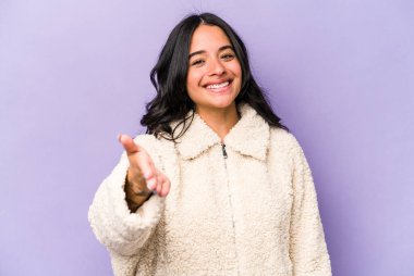 Mor arka planda izole edilmiş genç İspanyol kadın selamlama jesti olarak kameraya elini uzatıyor..