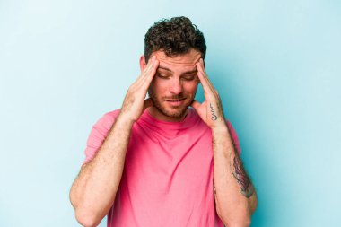 Genç beyaz adam mavi arka planda izole edilmiş tapınaklara dokunuyor ve başı ağrıyor..