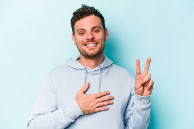 Kafkasyalı genç adam mavi arka planda izole edilmiş yemin ediyor, elini göğsüne koyuyor..