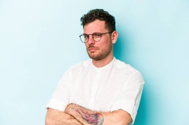 Kafkasyalı genç adam mavi arka planda izole edilmiş şüpheli, belirsiz, seni muayene ediyor..