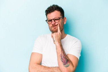 Mavi arka planda izole edilmiş genç beyaz adam alaycı bir ifadeyle kameraya bakarken mutsuz oluyor..