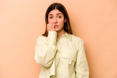 Genç İspanyol kadın bej arka planda izole edilmiş tırnaklarını yiyor, gergin ve çok endişeli..