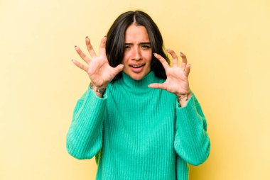 Sarı arka planda izole edilmiş genç İspanyol kadın gergin elleriyle çığlık atıyor..