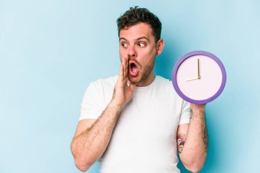 Mavi arka planda izole bir saat tutan genç beyaz adam gizli bir sıcak fren haberi söylüyor ve yana bakıyor