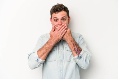 Beyaz arka planda izole edilmiş genç beyaz adam elleriyle ağzını kapatırken şok oldu..