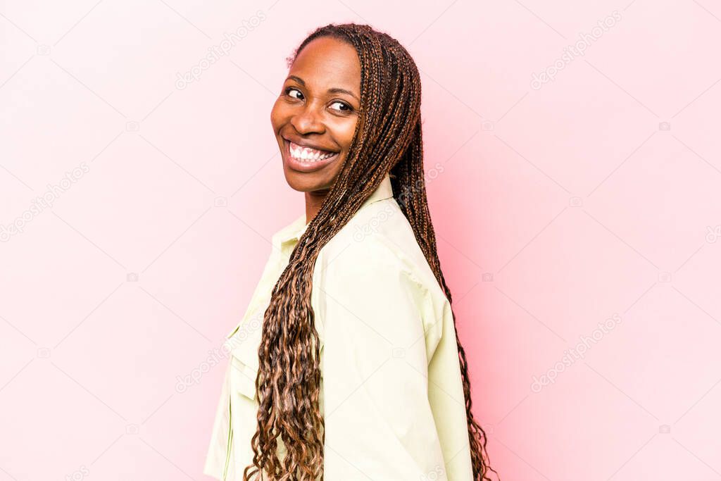 Young african american woman isolated on pink background looks aside smiling, cheerful and pleasant.