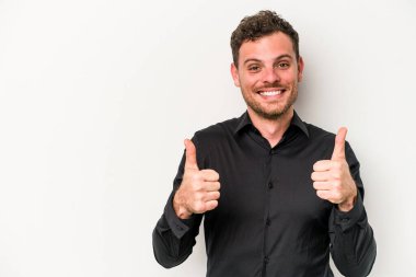 Beyaz arka planda izole edilmiş genç beyaz adam gülümsüyor ve başparmağını kaldırıyor.