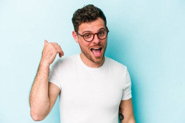 Mavi arka planda izole edilmiş genç beyaz bir adam bir şeye gülüyor, ağızlarını ellerle kapatıyor..