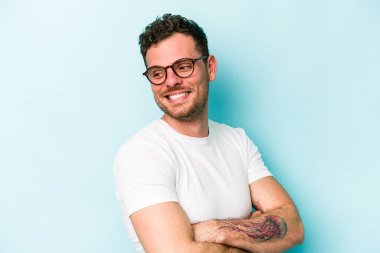 Kafkasyalı genç adam mavi arka planda izole edilmiş gülüyor ve eğleniyor..