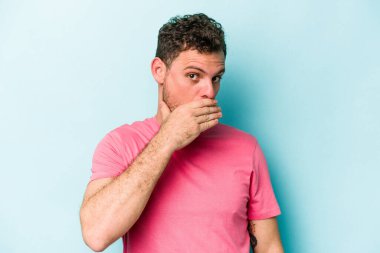 Kafkasyalı genç adam mavi arka planda izole edilmiş ağzı kapalı ve elleri endişeli görünüyor..