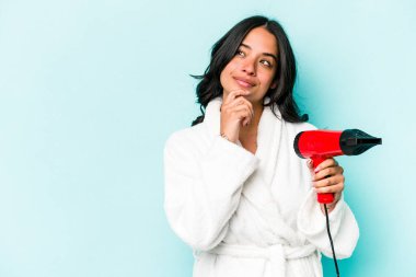 Kurutucuyu mavi arka planda tutan genç İspanyol kadın şüpheli ve şüpheci bir ifadeyle yana bakıyor..