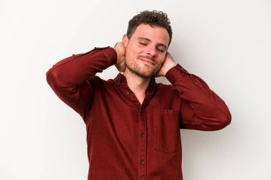 Beyaz arka planda izole olmuş genç beyaz bir adam kendini güvende hissediyor, elleri başının arkasında..