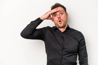 Beyaz arka planda izole edilmiş genç beyaz bir adam uzaklara bakıyor ve elini alnına koyuyor..