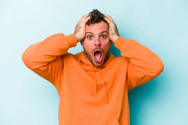 Genç beyaz adam mavi arka planda izole edilmiş bağırıyor, çok heyecanlı, tutkulu, bir şeyden memnun..